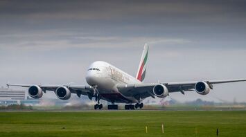 Emirates plane taking off from the runway under a cloudy sky near an airport terminal