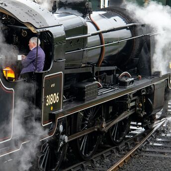 A heritage steam locomotive in operation with a fireman tending to the firebox, surrounded by steam