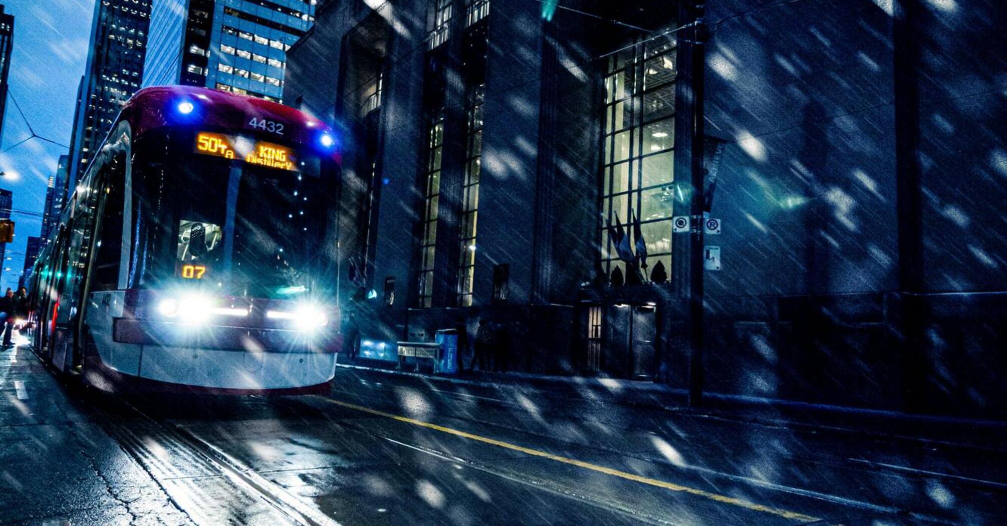 A tram navigating through a snowy city street at night