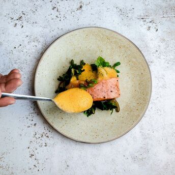 A gourmet dish featuring salmon with vibrant foam and greens on a minimalist plate
