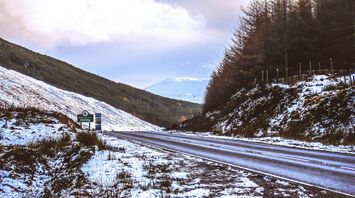 Snow-covered roadside in Scotland with a Stirling sign and distant hills under a cloudy sky