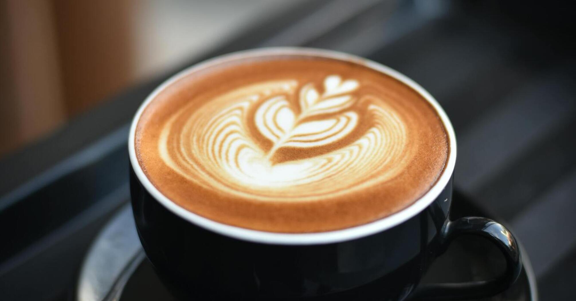 A cup of coffee with latte art in a black cup on a tray