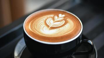 A cup of coffee with latte art in a black cup on a tray