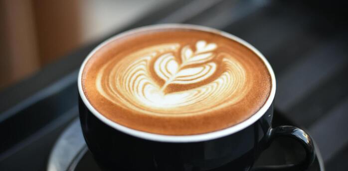 A cup of coffee with latte art in a black cup on a tray
