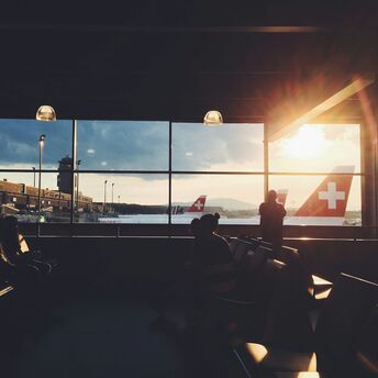A silhouette of passengers waiting in an airport lounge, with SWISS aircraft visible through large windows at sunset