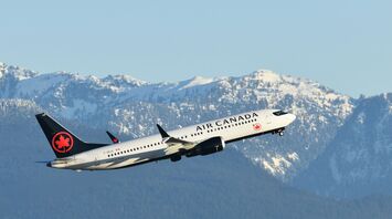 A white Air Canada plane takes off against a backdrop of snow-capped mountains under a clear blue sky