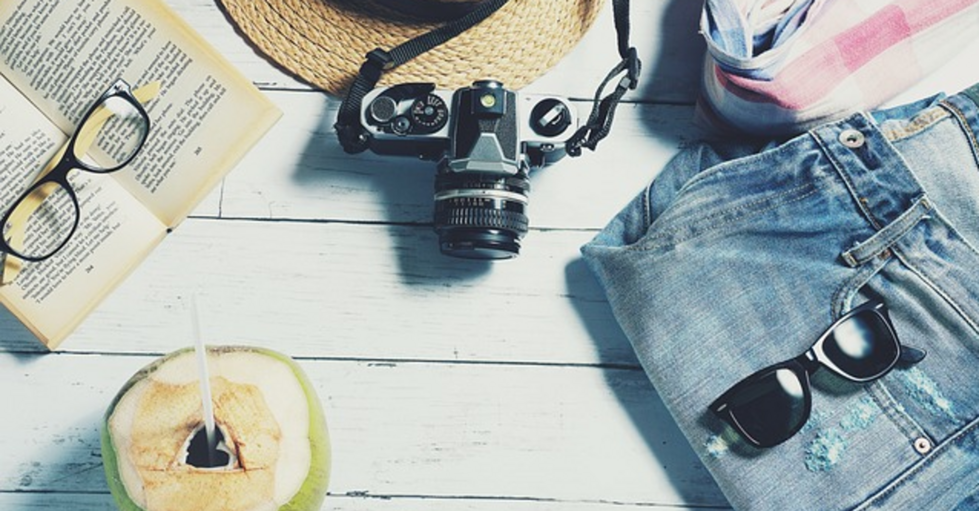 A summer vacation setting with sunglasses, a hat, a book, and a coconut on a table