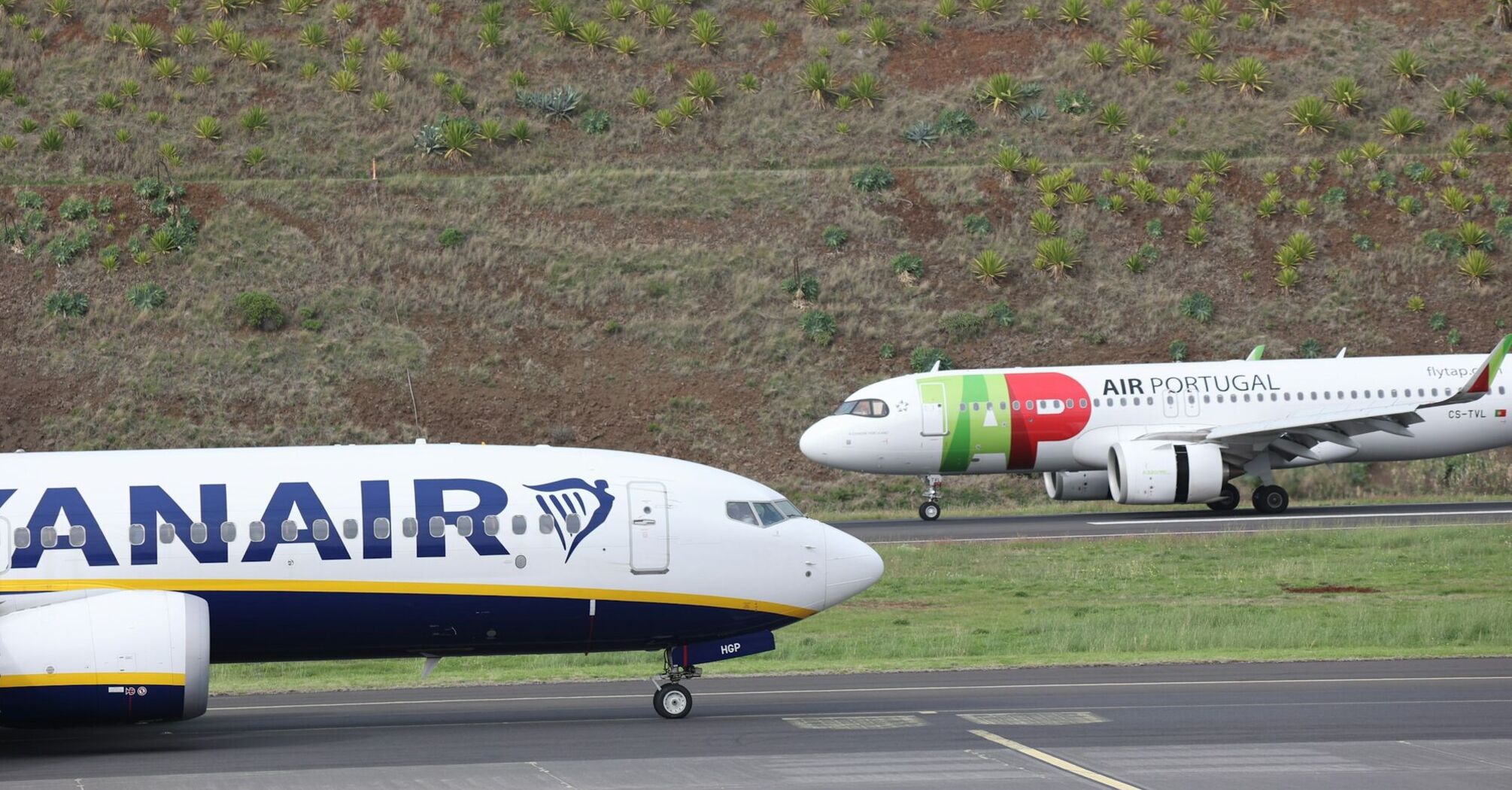 A TAP Air Portugal aircraft and a Ryanair plane on a runway surrounded by greenery