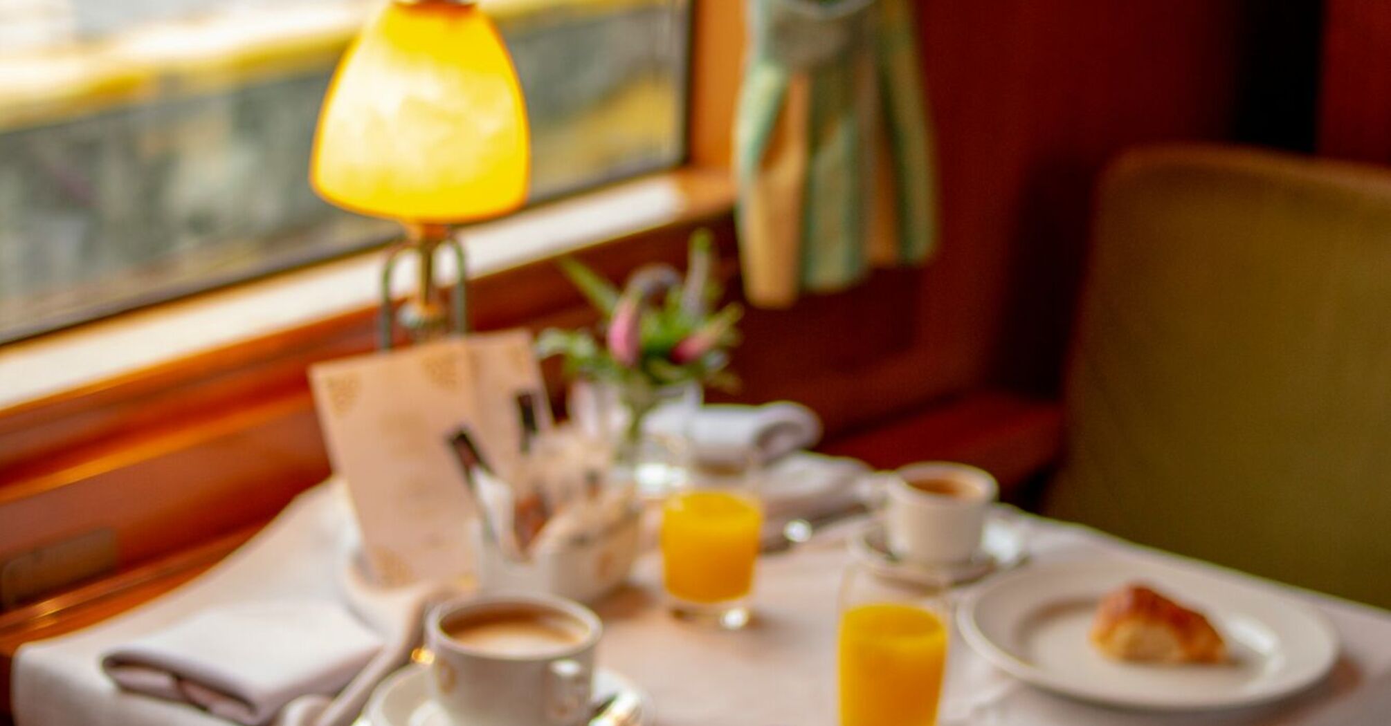 A luxurious dining setup with coffee, orange juice, and pastries inside a vintage train carriage