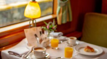 A luxurious dining setup with coffee, orange juice, and pastries inside a vintage train carriage
