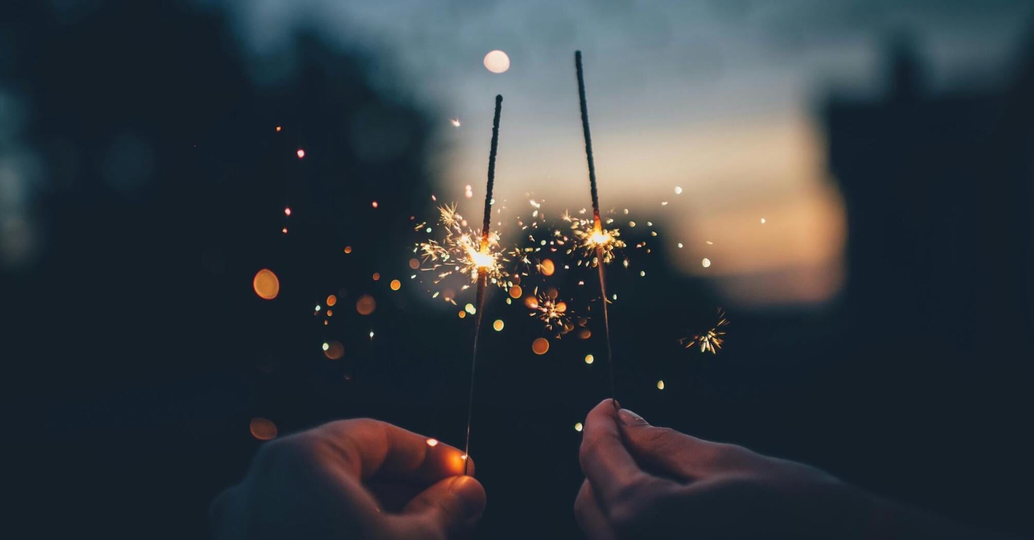 Two hands holding sparklers against a dark evening background