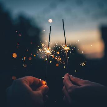 Two hands holding sparklers against a dark evening background