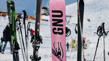 A collection of skis and snowboards on a snowy slope, with people and ski lifts in the background