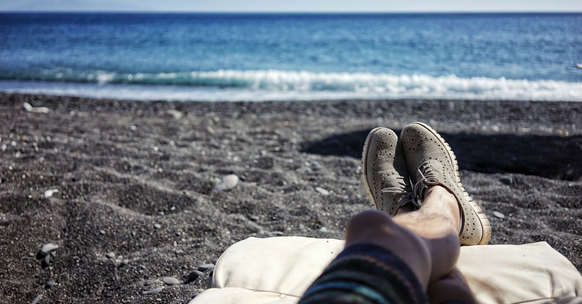 A relaxing view of the sea with legs resting on a beach chair and waves gently hitting the shore