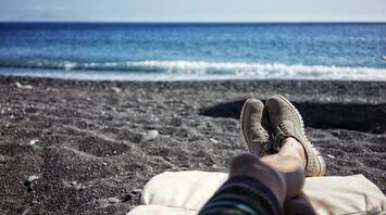A relaxing view of the sea with legs resting on a beach chair and waves gently hitting the shore