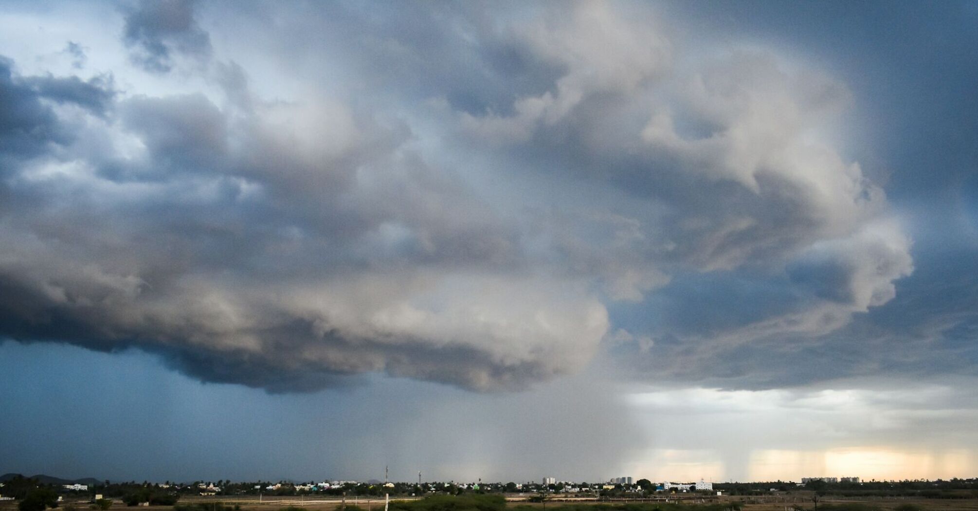 Dark storm clouds hover over a distant cityscape, signaling an impending heavy rainstorm