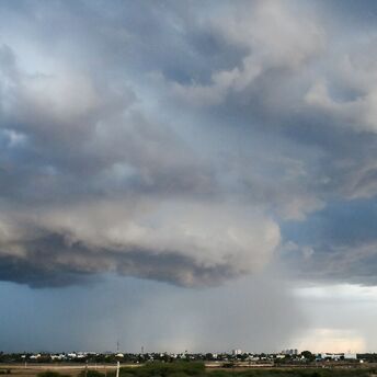 Dark storm clouds hover over a distant cityscape, signaling an impending heavy rainstorm