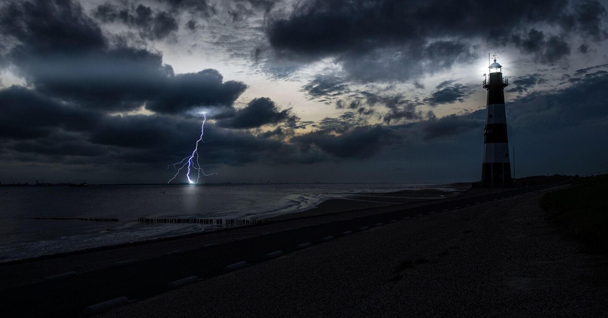 A lighthouse during a thunderstorm with lightning striking the sea