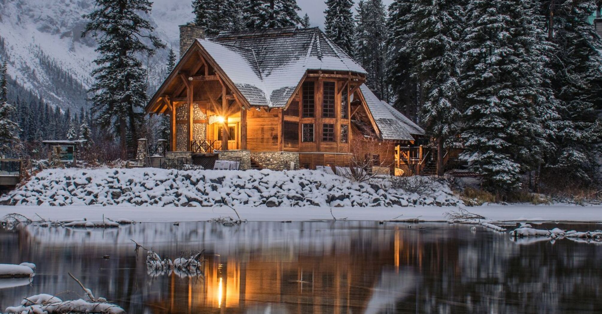 A cozy wooden cabin surrounded by snow-covered trees, reflected in a calm winter lake