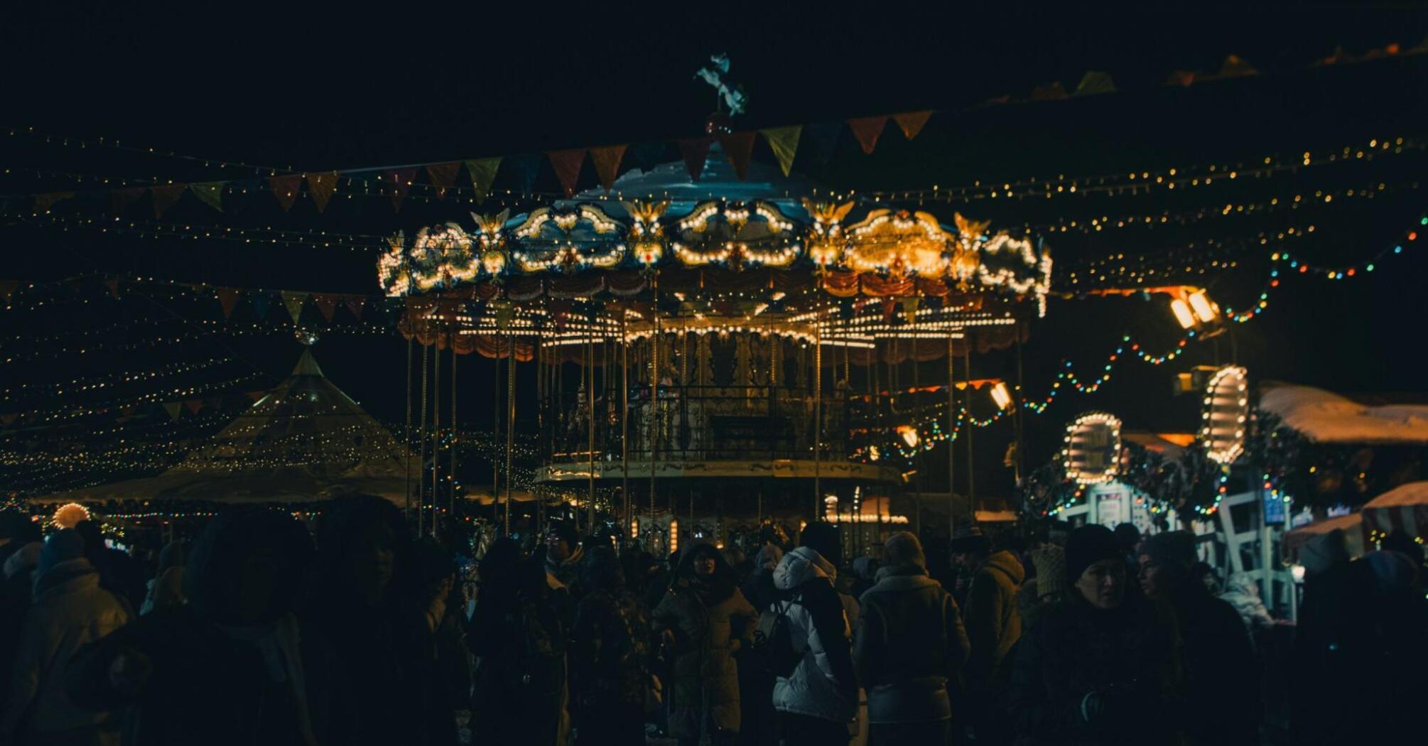 A festive evening market with a carousel, lights, and people enjoying the atmosphere