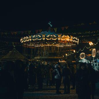 A festive evening market with a carousel, lights, and people enjoying the atmosphere