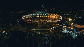A festive evening market with a carousel, lights, and people enjoying the atmosphere