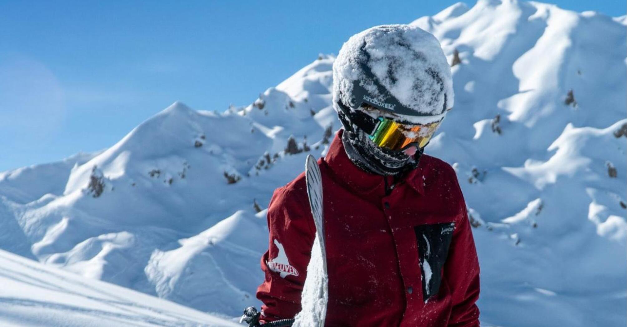 A snowboarder standing in deep snow surrounded by majestic snowy mountain peaks