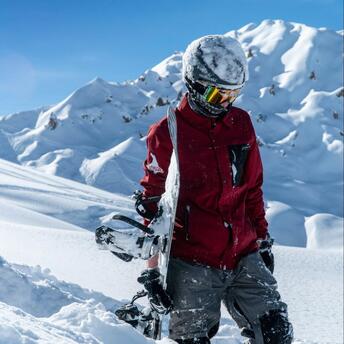 A snowboarder standing in deep snow surrounded by majestic snowy mountain peaks