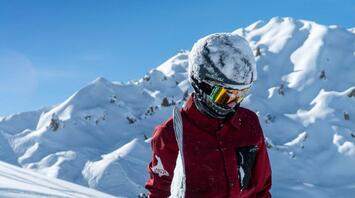 A snowboarder standing in deep snow surrounded by majestic snowy mountain peaks