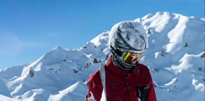 A snowboarder standing in deep snow surrounded by majestic snowy mountain peaks