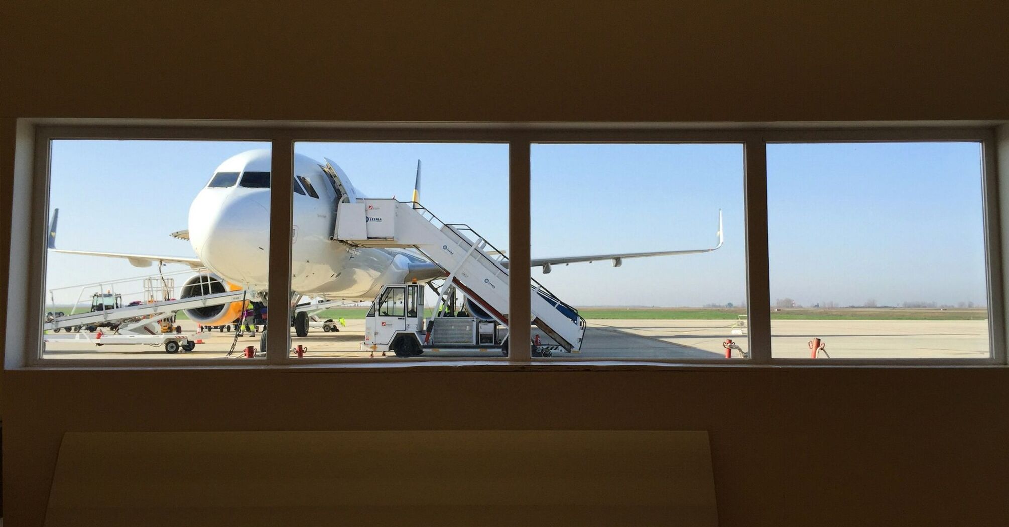 A large airplane viewed through an airport window with a boarding staircase attached on the tarmac