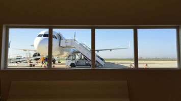 A large airplane viewed through an airport window with a boarding staircase attached on the tarmac