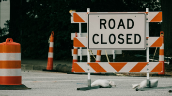 A road closed sign with orange traffic barrels and barricades indicating a blocked roadway