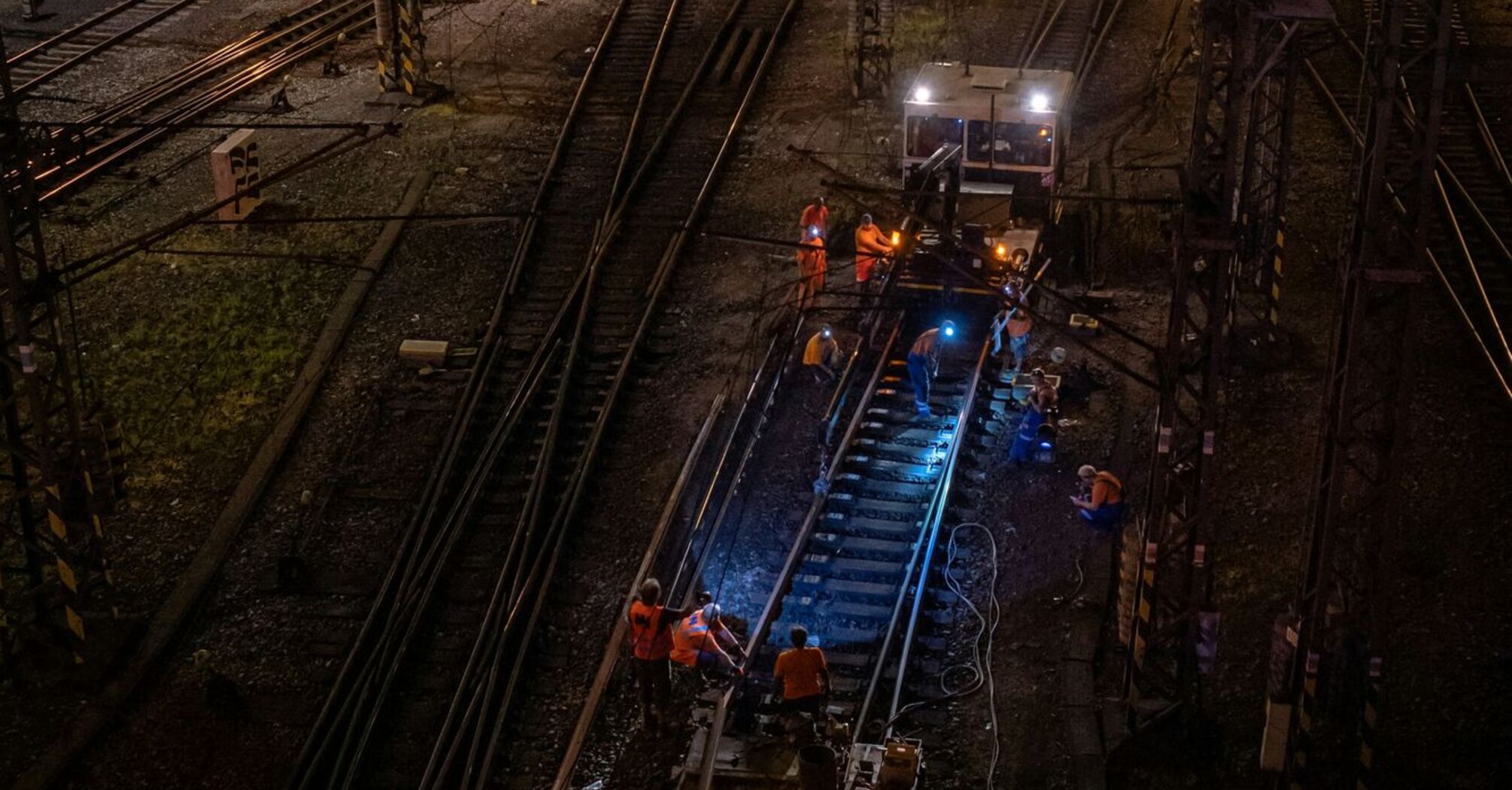 Rail workers repairing damaged train tracks at night under bright lights