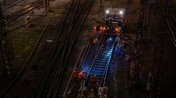 Rail workers repairing damaged train tracks at night under bright lights