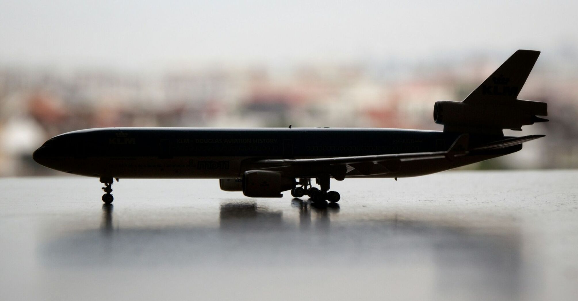Silhouette of a model airplane against a blurred cityscape