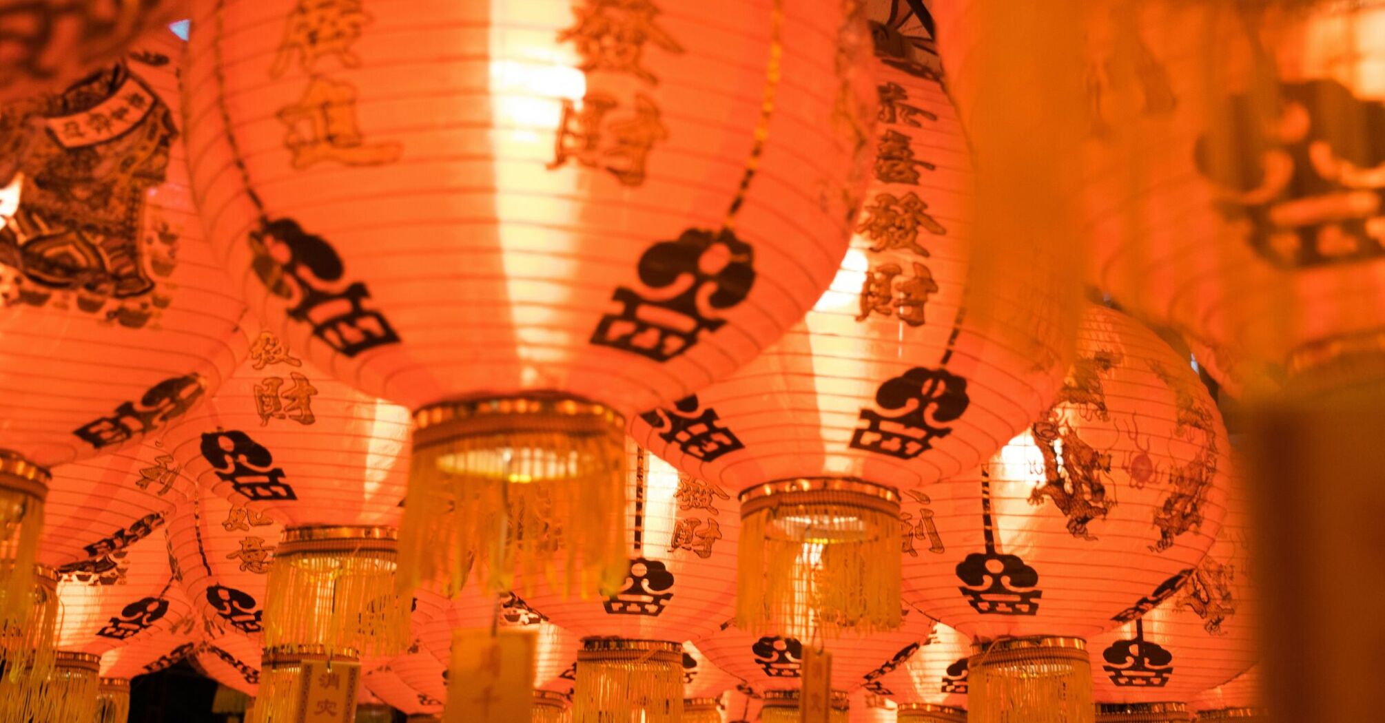 Red Chinese lanterns illuminated from within, with decorative patterns and Chinese characters, hanging closely together