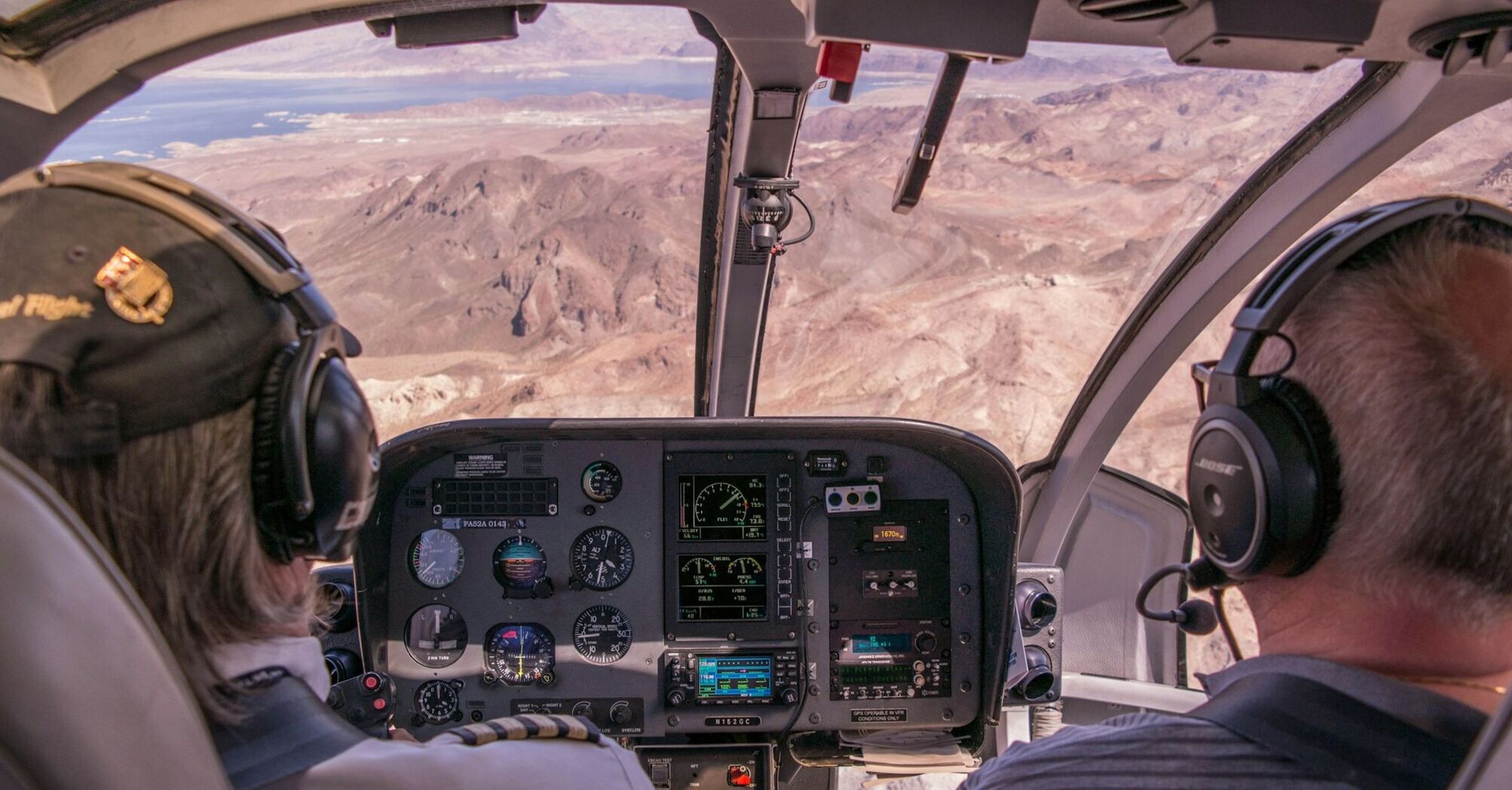 Two pilots control an airplane, view from the cockpit to the mountainous landscape beyond