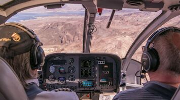 Two pilots control an airplane, view from the cockpit to the mountainous landscape beyond