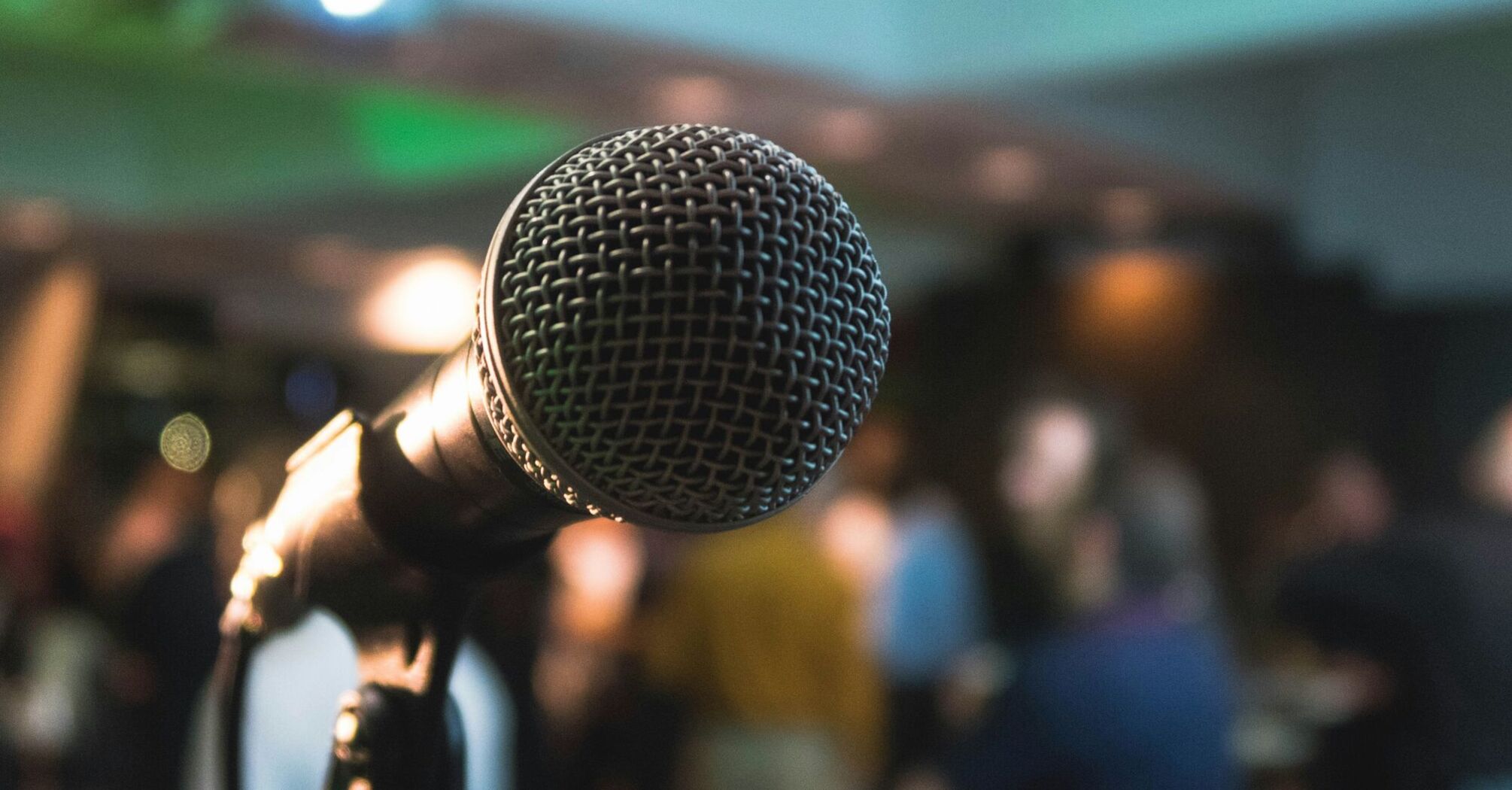 A close-up of a microphone in focus with a blurred background of people in a conference setting