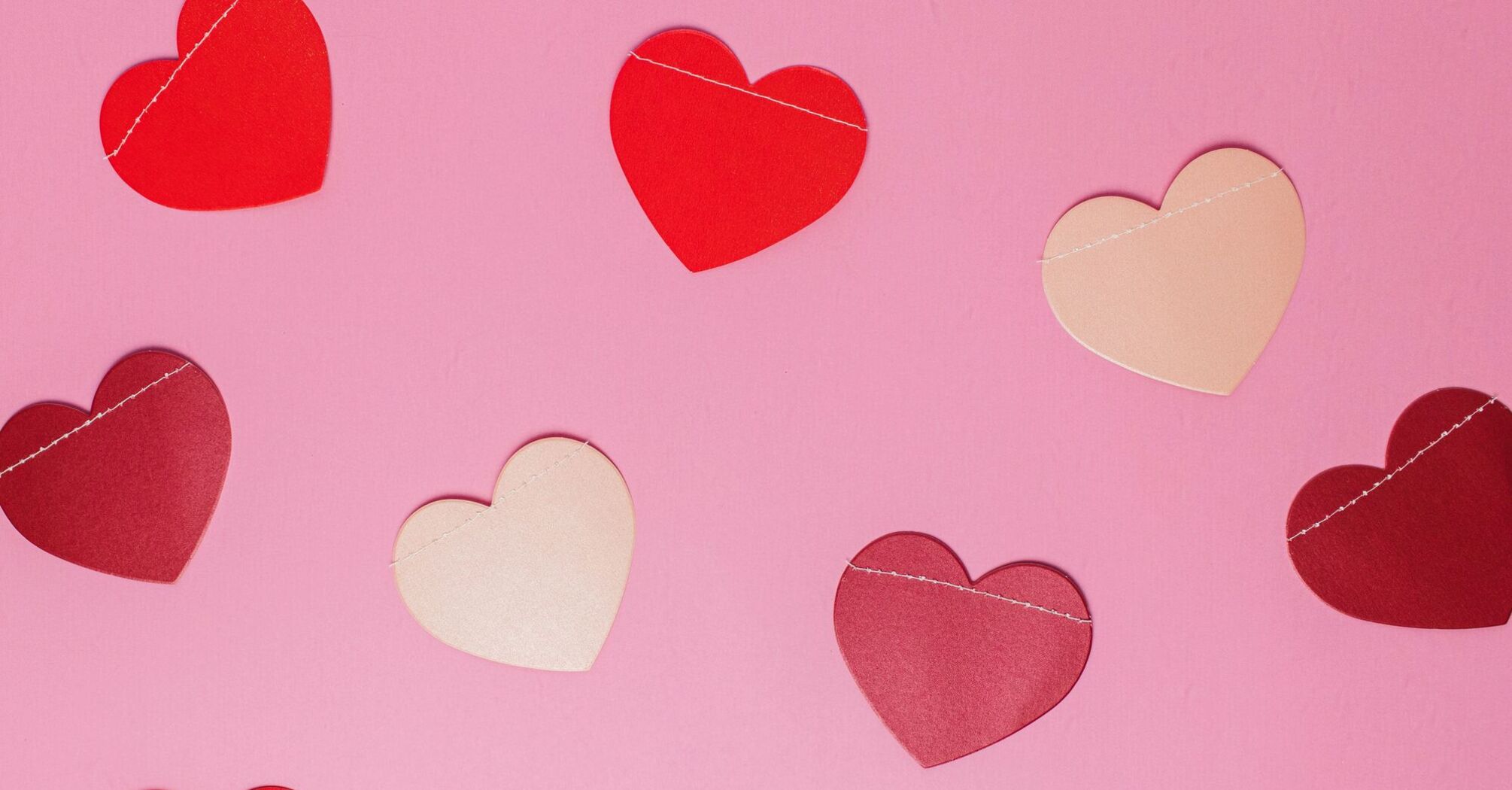 Assorted paper hearts in shades of red and pink scattered on a plain pink background