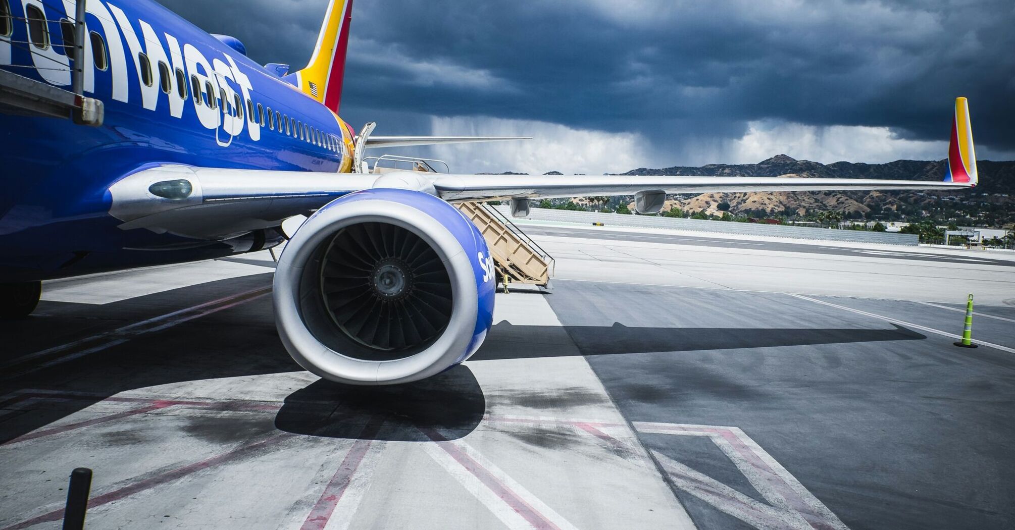 Southwest Airlines aircraft parked at an airport gate with the boarding stairs attached, under a stormy sky