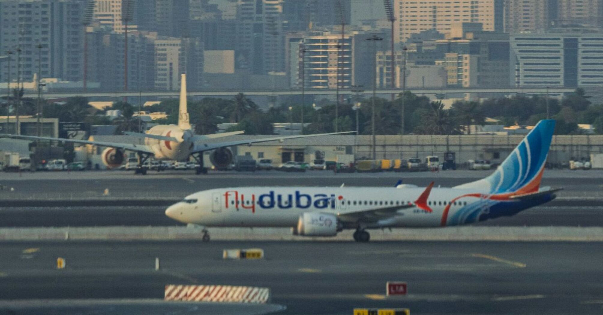 A flydubai aircraft on the tarmac Airport with the city's skyline in the background during dusk