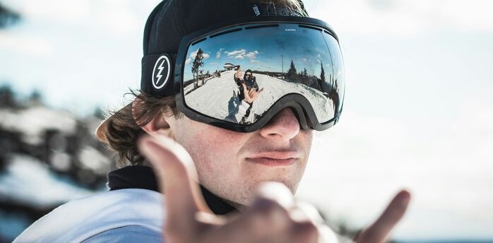 A person in a ski cap and goggles making a peace sign