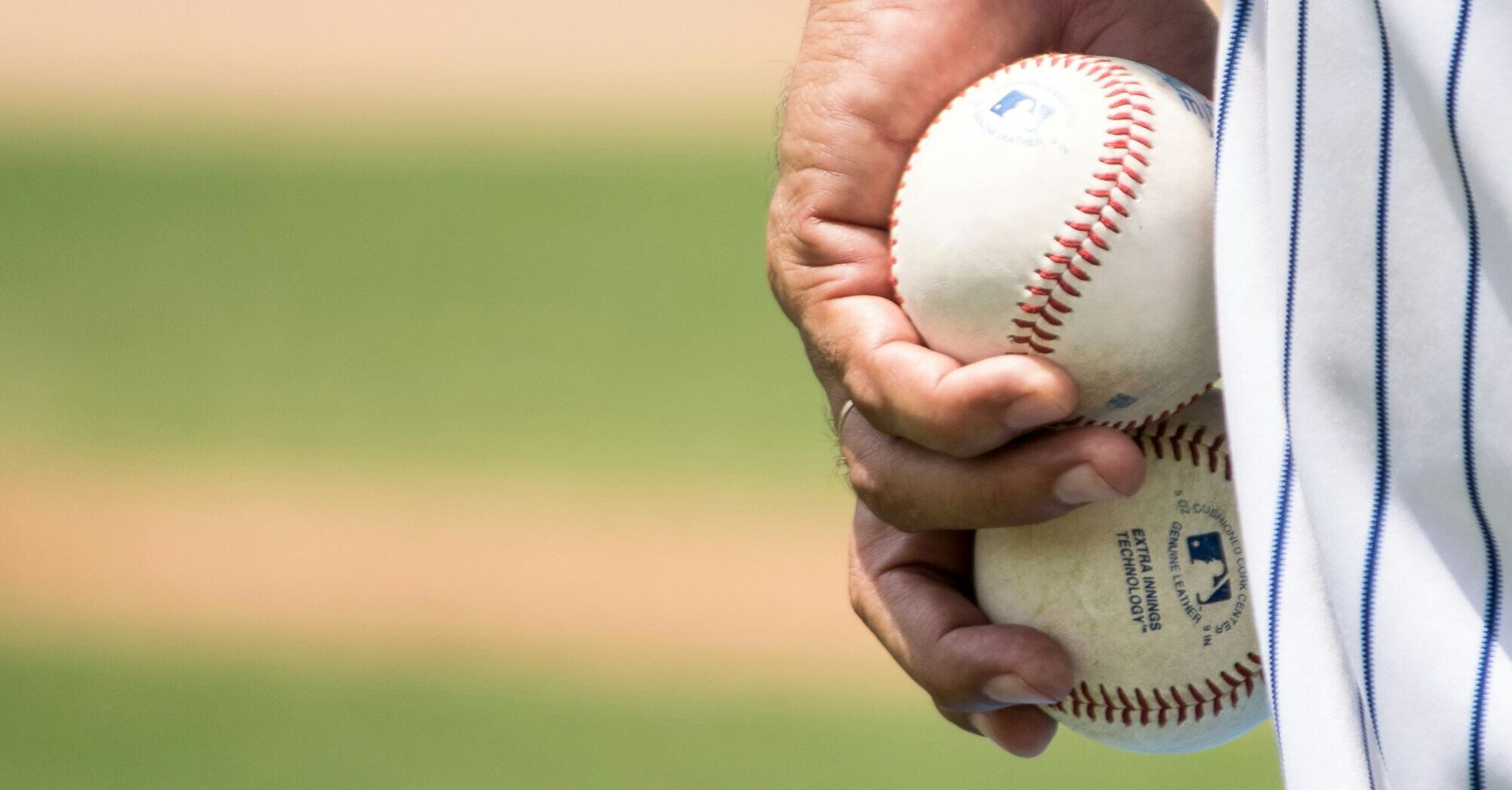 A close-up of a hand holding a baseball with the Major League Baseball logo visible 