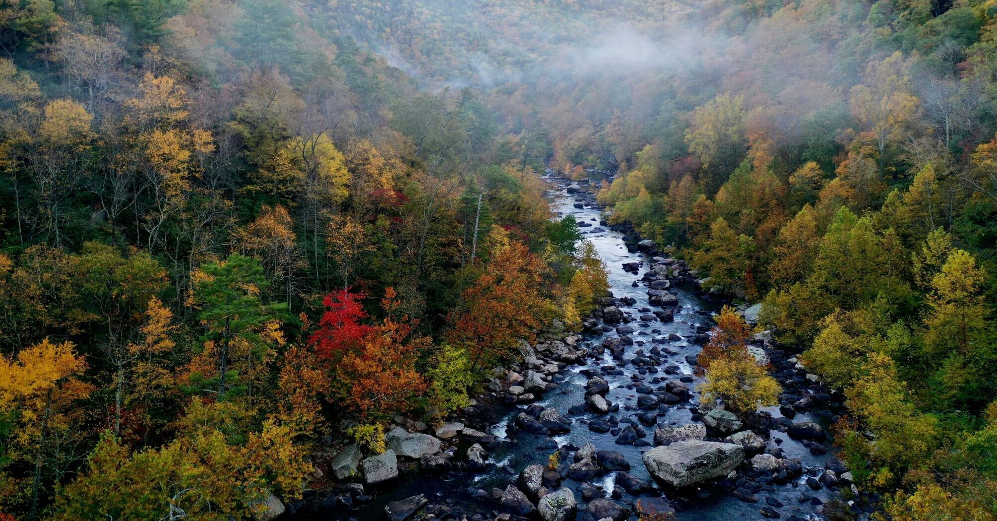 River runs through fall trees in valley with clouds