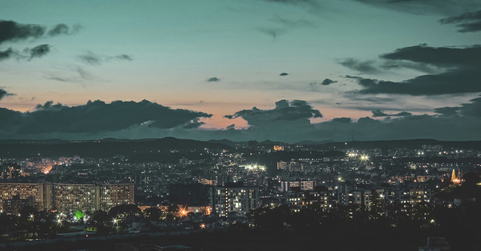 A twilight view of Pune cityscape with illuminated buildings against a backdrop of hills and a cloudy sky