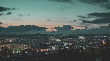 A twilight view of Pune cityscape with illuminated buildings against a backdrop of hills and a cloudy sky