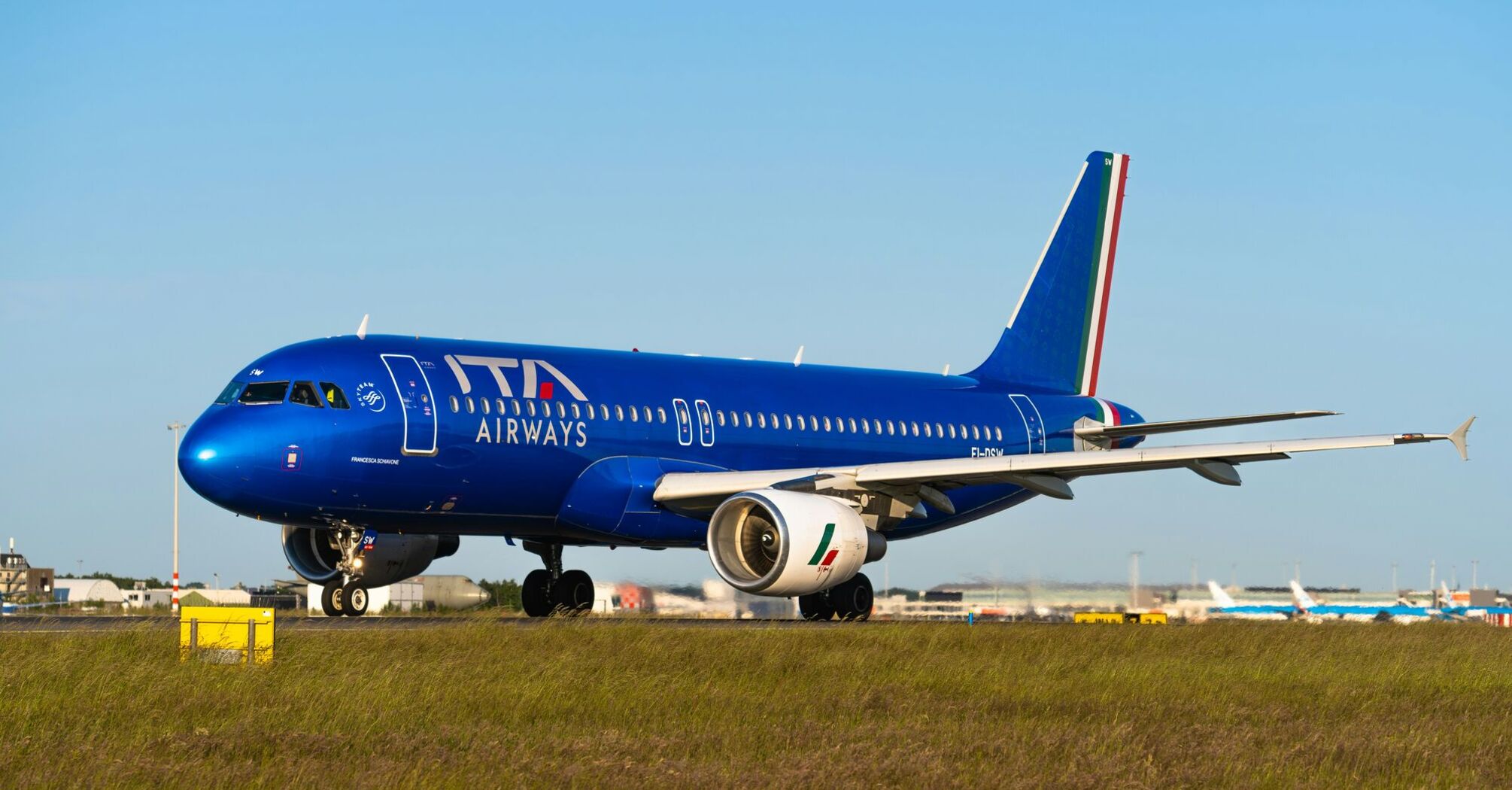 ITA Airways aircraft on the tarmac with blue livery and Italian flag on the tail 