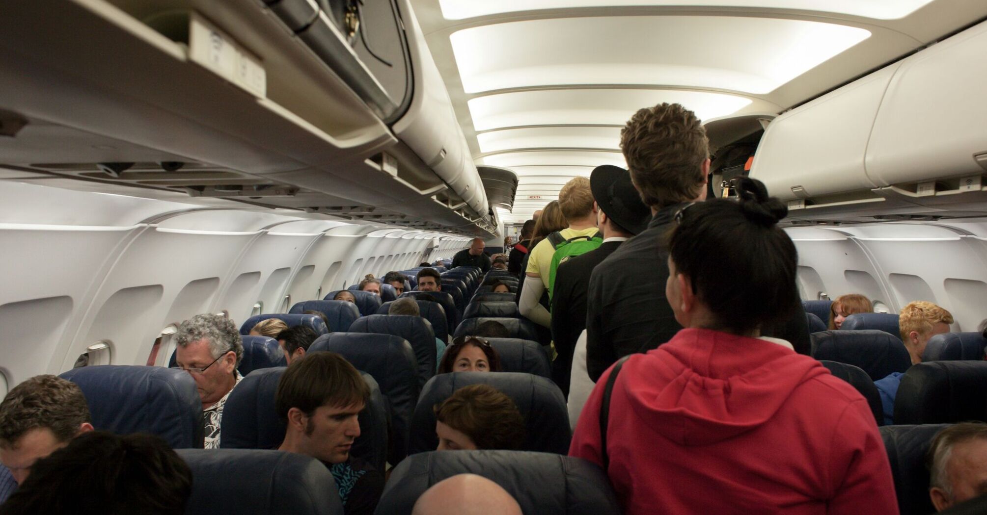 Passengers standing in the aisle of an airplane, waiting to take their seats
